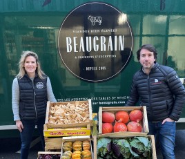 une femme et un homme encadrent des caisses de fruits et légumes
