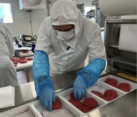 opérateur en blouse blanche et gants bleus devant des steaks hachés en barquettes
