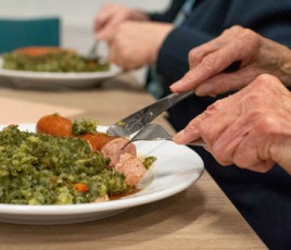 Personne agée qui mange à table des petits pois carottes et viande