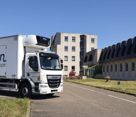 un camion stationné en épi sur une route avec des immeubles en fond.