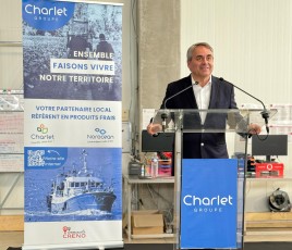 Au premier plan, un homme souriant fait un discours au pupitre ; une affiche au second plan. 