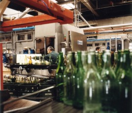 Des bouteilles en verre au premier plan sur une ligne d'embouteillage et un opérateur au deuxième plan.