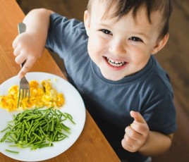 un enfant à table avec sa fourchette et une assiette