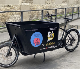 vélo cargo noir arrêté dans une rue. Logo bleu avec éléphant rose sur la caisse. 