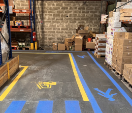 marquages jaune et bleu pour la circulation des hommes et des engins de manutention au sol d'un entrepôt. Mur en briques au fond.