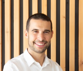 jeune homme souriant en chemise blanche. Sur fond bois.