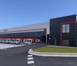Un entrepôt avec de nombreux camions garés devant. Un carré de gazon sur la droite.