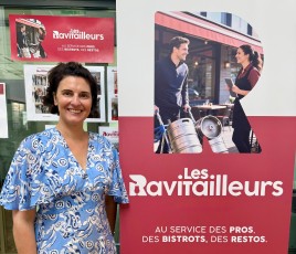 Une femme, brune, en robe bleu clair, debout à côté d'un kakémono rouge et blanc. 