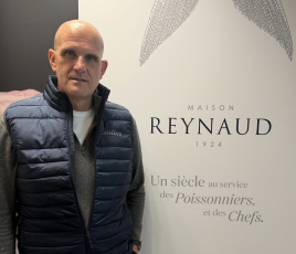 un homme chauve, habillé en bleu marine, debout à côté d'un kakemono d'entreprise 