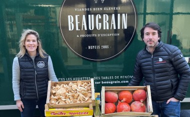 une femme et un homme encadrent des caisses de fruits et légumes