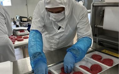 opérateur en blouse blanche et gants bleus devant des steaks hachés en barquettes