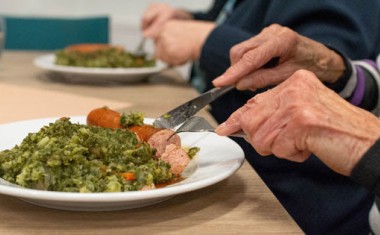 Personne agée qui mange à table des petits pois carottes et viande