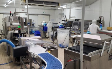 Ligne de conditionnement avec un tapis bleu au premier pan et un opérateur au fond à droite de l'image.