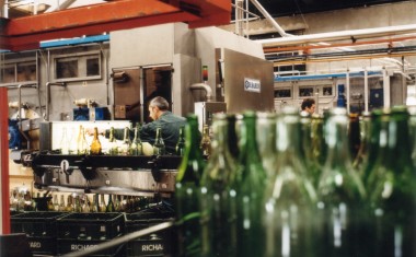 Des bouteilles en verre au premier plan sur une ligne d'embouteillage et un opérateur au deuxième plan.
