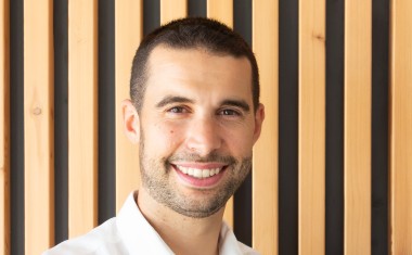 jeune homme souriant en chemise blanche. Sur fond bois.