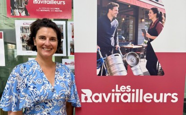 Une femme, brune, en robe bleu clair, debout à côté d'un kakémono rouge et blanc. 