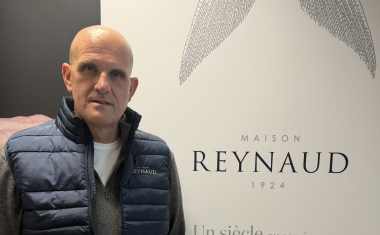 un homme chauve, habillé en bleu marine, debout à côté d'un kakemono d'entreprise 