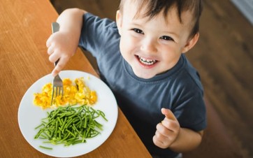 un enfant à table avec sa fourchette et une assiette