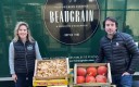 une femme et un homme encadrent des caisses de fruits et légumes