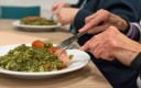 Personne agée qui mange à table des petits pois carottes et viande