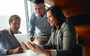 Une femme et deux hommes en réunion autour d'une tablette dans une entreprise.