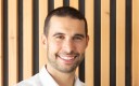 jeune homme souriant en chemise blanche. Sur fond bois.