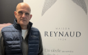 Sur la gauche de l'image : un homme chauve vêtu d'une doudoune bleue; A sa gauche, un kakémono sur fond blanc. 
